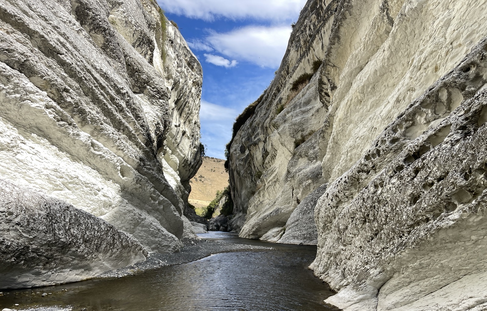 A narrow gorge of pale water-carved limestone, a river running along its floor under a blue sky.