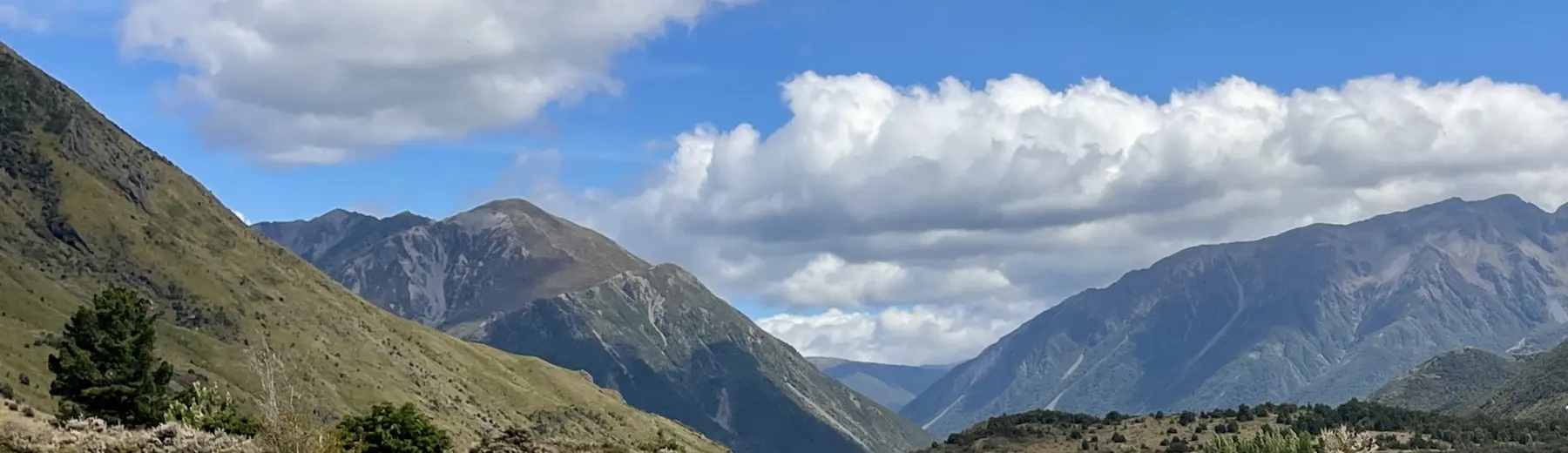 A wide braided river valley between bush-covered ranges under high cloud