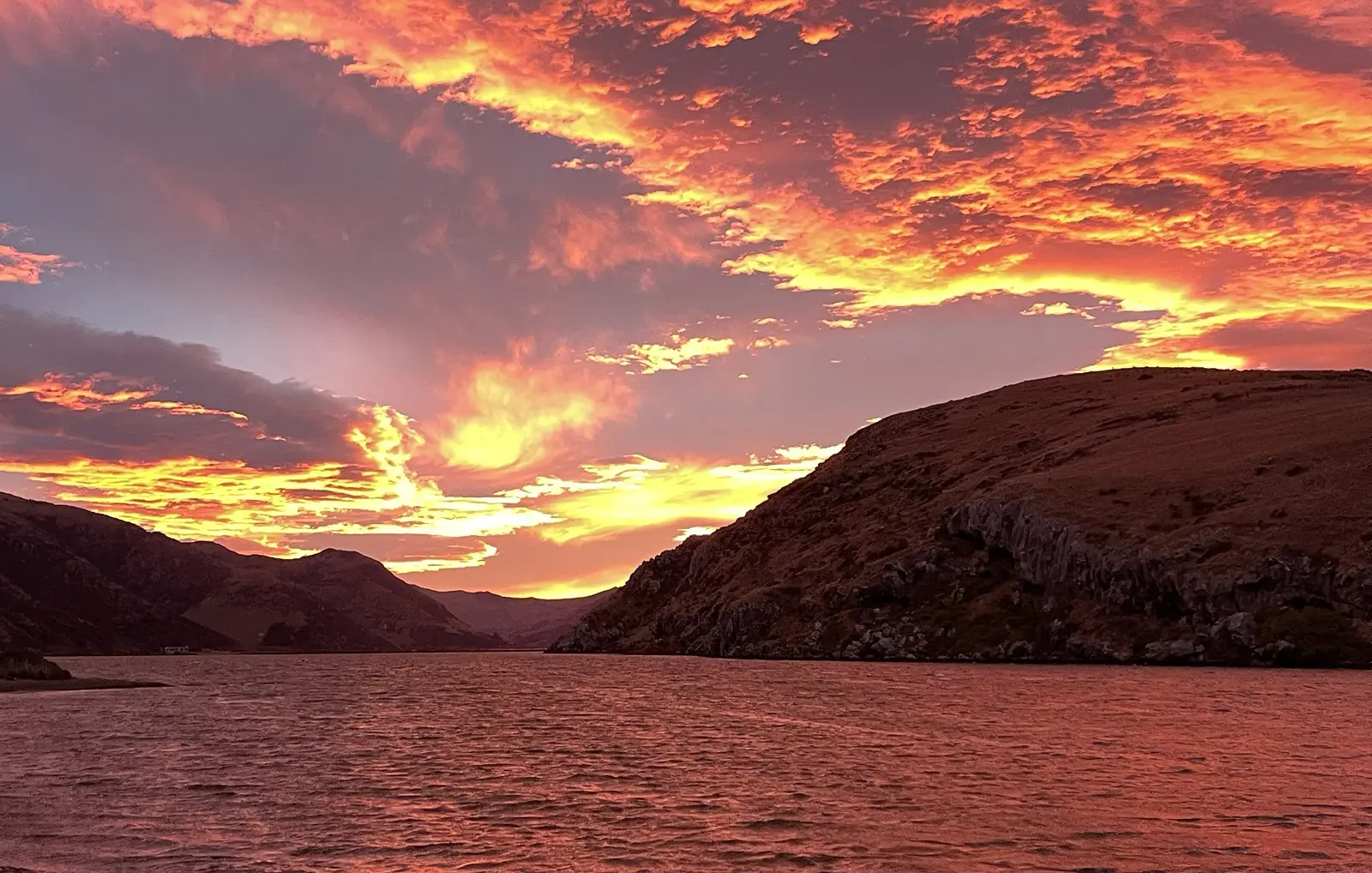 A fiery sunset over a harbour and hills, Aotearoa New Zealand